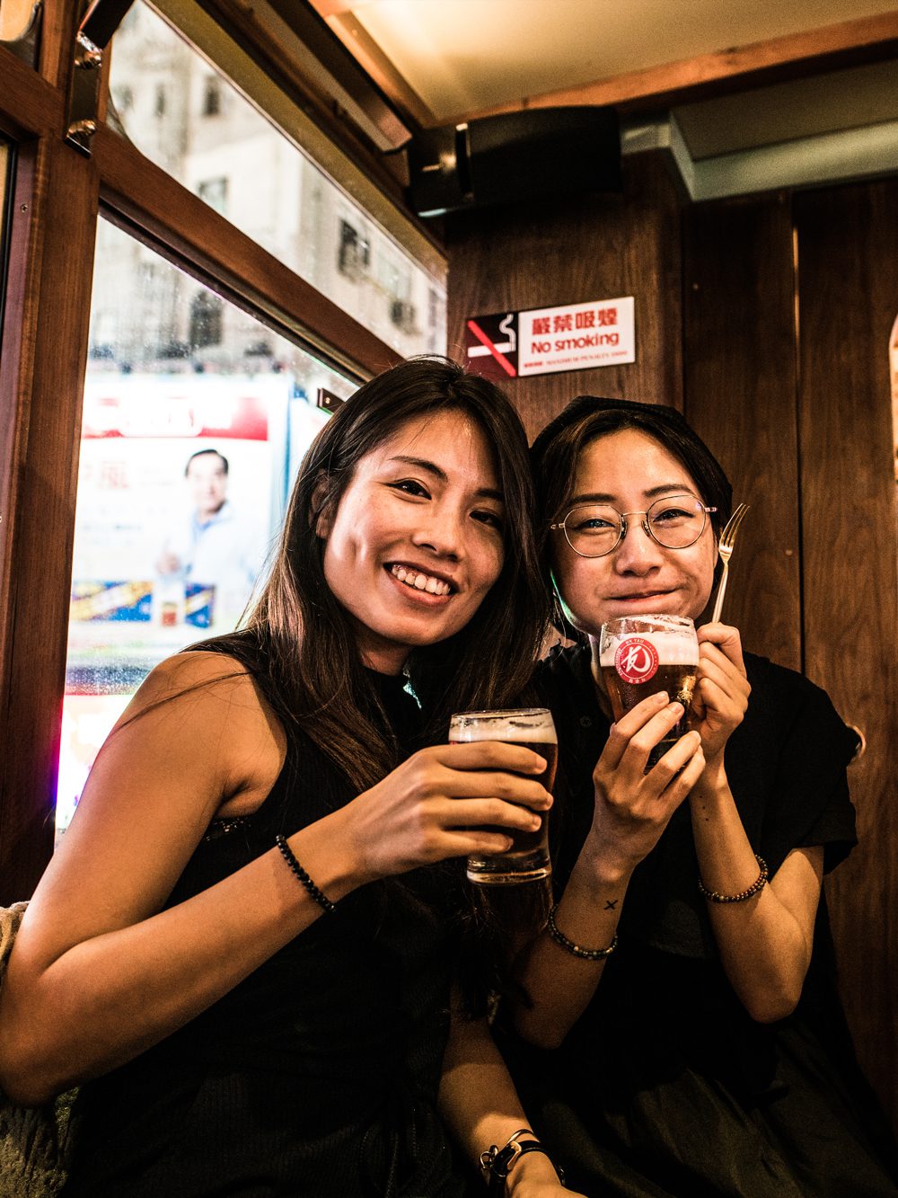 Two young ladies holding pints of HK YAU beer and smiling at the camera during an event on tram