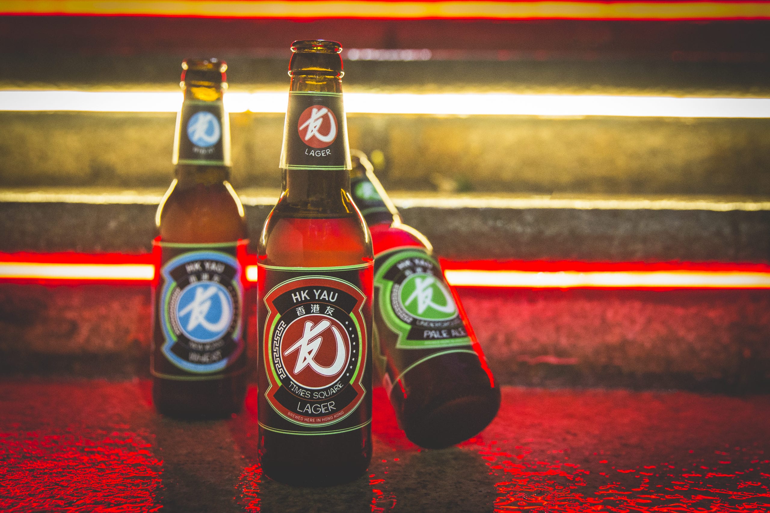 Three bottles of craft beer on the floor with neon lights on behind