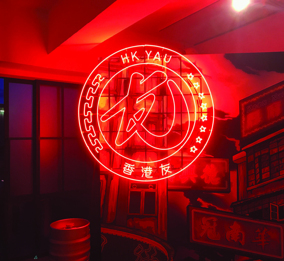 Red neon HK YAU logo designed by ipulse creative agency Hong Kong overlays on top of an interior image of a craft beer warehouse in Hong Kong
